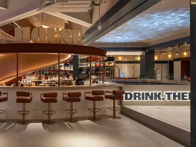A modern restaurant bar with a concrete floor and wooden bar stools.