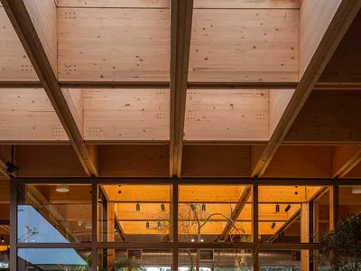 A modern, industrial-style restaurant interior with wooden structural beams and large glass windows.