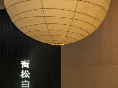 A modern restaurant interior with wooden walls and a large paper lamp hanging overhead.