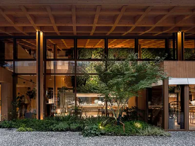 A modern restaurant exterior featuring a wooden and glass facade with greenery.