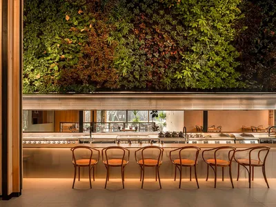 Modern restaurant interior featuring green vertical garden walls, wooden furniture, and a central bar counter.
