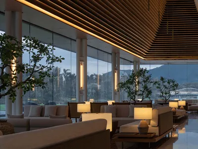 A modern hotel lobby with wooden paneling and glass walls, featuring comfortable seating arrangements and natural lighting.