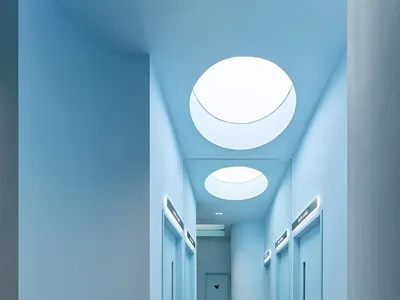 A minimalist hotel corridor with glass walls and ceiling lights.