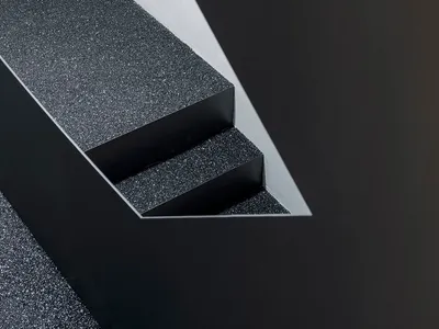 A close-up of a black granite staircase with textured steps and a contrasting wall.