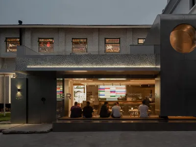 一群人坐在現代工業風餐廳外，混凝土牆面搭配玻璃窗