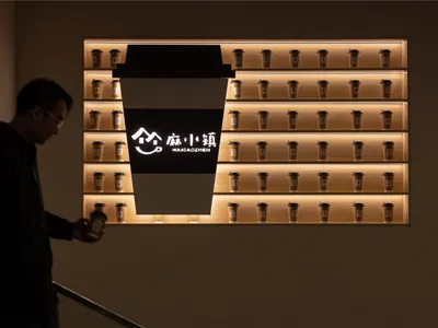 A coffee shop display featuring a large, illuminated coffee cup sign and numerous smaller coffee cups on shelves.
