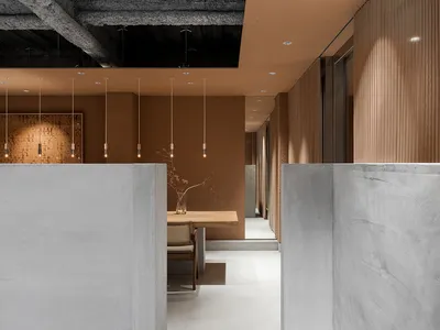 A modern restaurant interior features a textured concrete ceiling with minimal overhead lighting and a wooden dining table.