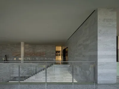 A modern hotel lobby featuring marble walls and floors, with a staircase and glass railings.