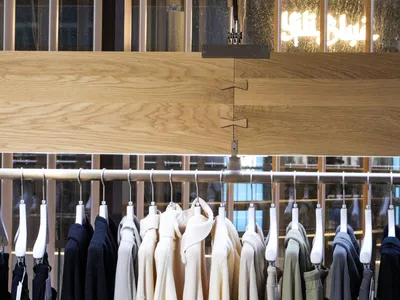 服飾店展示區以木質與金屬元素呈現，吊軌上懸掛各式服裝。