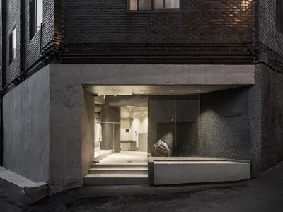 Concrete storefront with glass door and steps leading into a warmly lit interior.