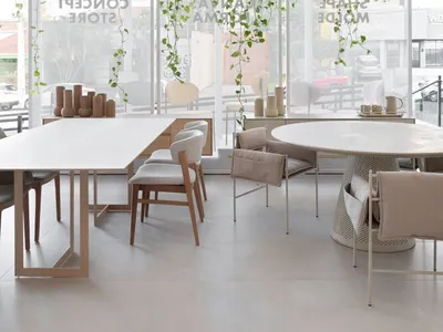 Modern cafe interior with white tables and chairs, wood composite flooring, and green hanging plants.