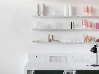 A minimalist home office featuring white shelves and chairs with green upholstery.