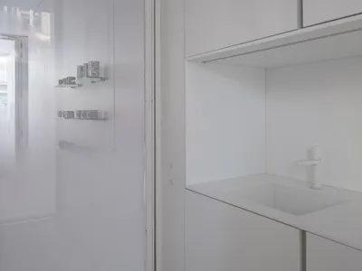 A minimalist white kitchen with white tiles, clean lines, and a white countertop.