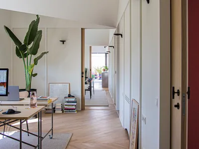 A modern home office with wooden flooring and walls, featuring a desk with a laptop and a green potted plant.