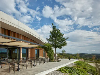 Outdoor seating area with tables and chairs on a wooden deck overlooking scenic hills.