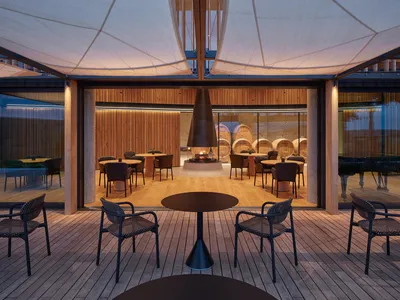 Modern restaurant interior with a central fire pit and wooden tables and chairs.