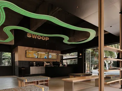 Industrial-style restaurant interior with concrete walls and floor, green neon decor, and seating areas