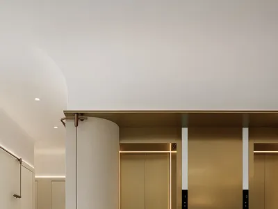 A modern minimalist hotel lobby featuring metallic brass finishes and a cylindrical column.