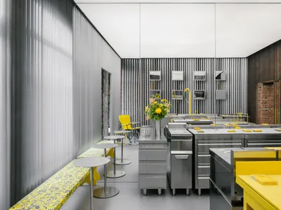 Modern minimalist restaurant kitchen featuring metal counters, wooden panels, and yellow accents.