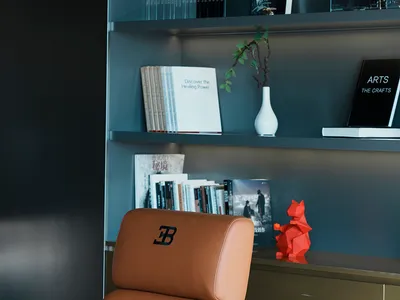 A modern home office featuring a sleek bookshelf with a beige leather chair and various books and decorative items.