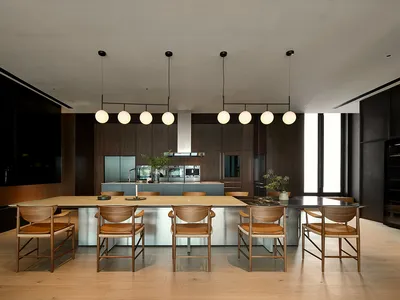 A modern residential kitchen featuring wooden chairs, glass countertops, and stainless steel appliances.
