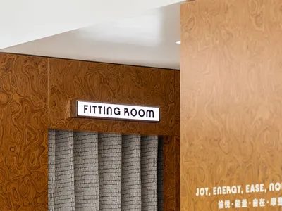 Close-up of a fitting room with a wood-textured wall and a gray curtain in a fashion retail store.