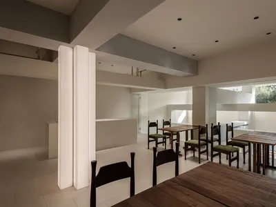 A modern minimalist restaurant interior featuring wooden tables and chairs.