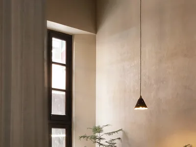 A cozy restaurant interior featuring a wooden table with a yellow cushion, green plants, and a hanging pendant light.