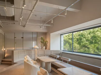 Modern restaurant interior with white seating, tall table, and large window overlooking greenery.