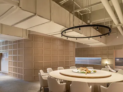 Modern restaurant dining area with a circular table surrounded by white chairs and a neutral-toned wall.