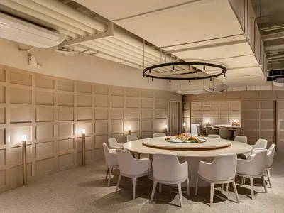 A modern restaurant with a circular table surrounded by white chairs, featuring wooden paneling walls and a circular light fi