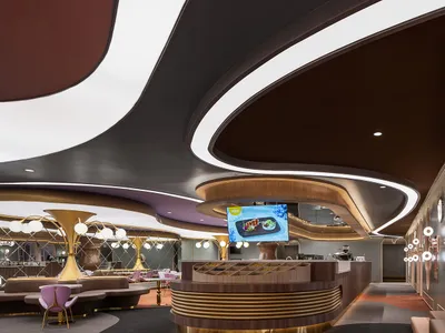 A modern restaurant bar with brass and glass accents, featuring a circular bar counter and large, curved ceiling lights.