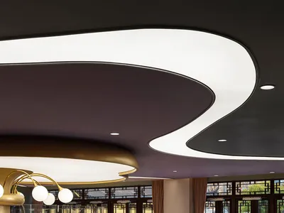 A modern restaurant interior with white and gold lighting fixtures, purple chairs, and a mix of soft surfaces and glass parti