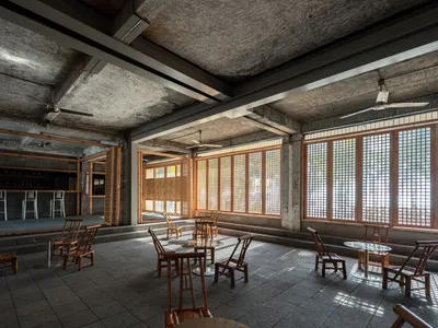 Industrial-style restaurant bar with concrete walls, wooden furniture, and large windows.