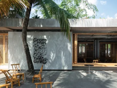 Modern minimalist restaurant exterior with concrete walls and open seating area under palm trees.