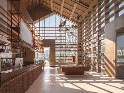 A modern interior featuring a restaurant, bar, and library with walls of wood and concrete, full-height glass windows, and pe