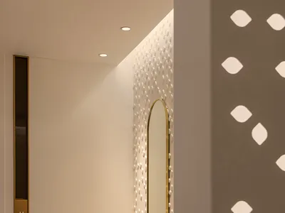 A modern hotel suite with white furniture, a vanity area with an oval mirror and decorative lighting, and a textured carpet.