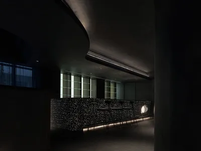 A minimalist modern cafe bar featuring a sleek concrete tile bar counter with integrated lighting and a unique circular table