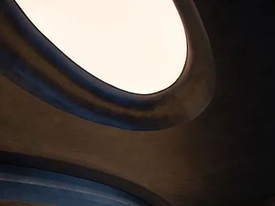 Modern hotel lobby interior featuring a sleek, curved concrete reception desk with a skylight overhead.