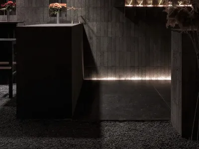 Dark, modern, concrete-themed restaurant-bar interior with minimalist design elements and warm lighting.