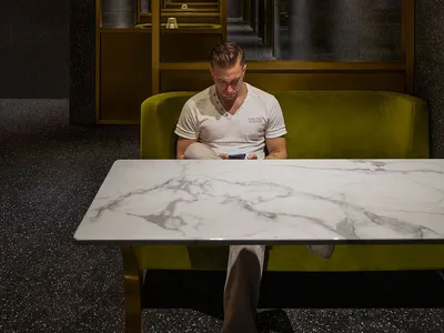 Man sitting at a modern cafe with black and golden metallic furniture, white marble table, and decorative lighting.