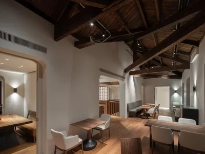 Interior view of an industrial-style restaurant dining room with wooden tables and chairs, featuring exposed wooden beams and