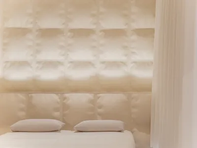 A minimalist bedroom featuring white fabric on the bed and wall panels.