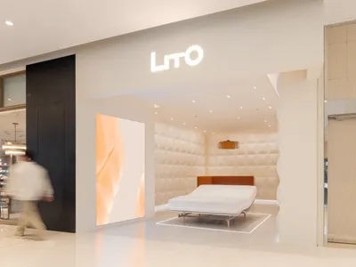 A modern bedroom showcasing a brown upholstered bed against a soft-textured fabric wall, illuminated by ceiling lights, with