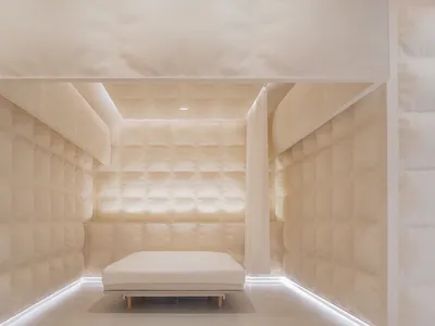 A minimalist bedroom with fabric walls, a single white mattress on a wooden platform, and ambient lighting.