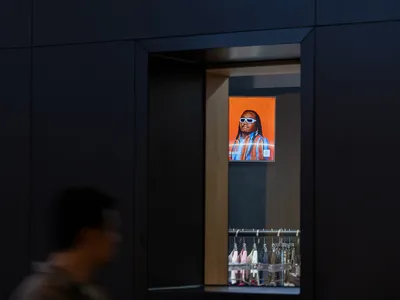 A digital retail display featuring a man with dreadlocks in sunglasses, backlit by an orange background.