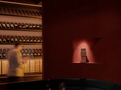 A cozy dining setup featuring a table with a bottle of wine and glasses, surrounded by upholstered seating and a terrazzo cou