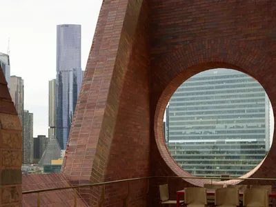 A rooftop lounge area with brick walls, a red circular table, and brown sofas and chairs.