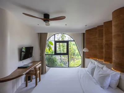 A minimalist bedroom featuring a white bed with a wicker headboard and wooden desk area.