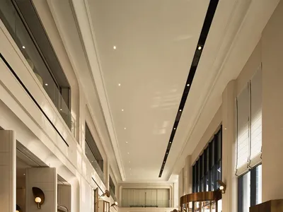 A spacious hotel lobby featuring modern lighting, concrete finishes, and glass details.